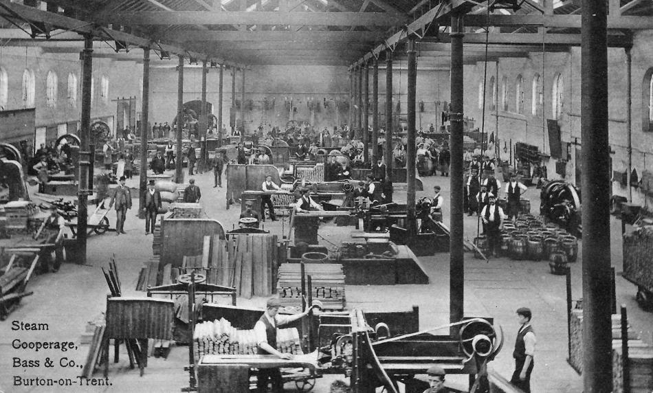 A black and white photograph of the inside of a 19th century working brewery with machinery and coopers.