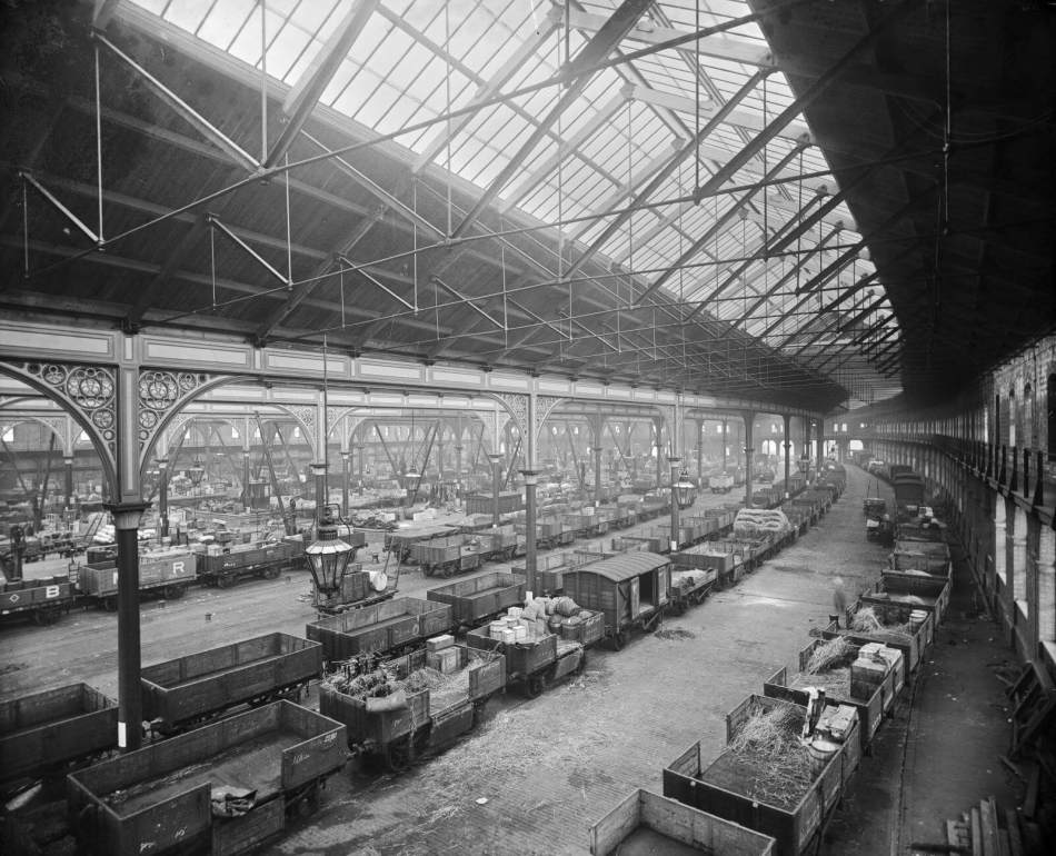 A black and white photograph of the interior of a massive goods shed.