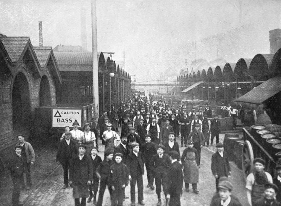 A black and white photograph of workers outside at a brewery.