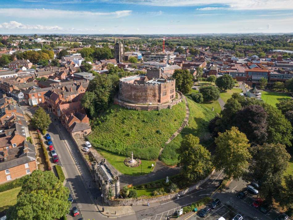 A photograph of a small castle on a hill, surrounded by modern housing, buildings and roads.