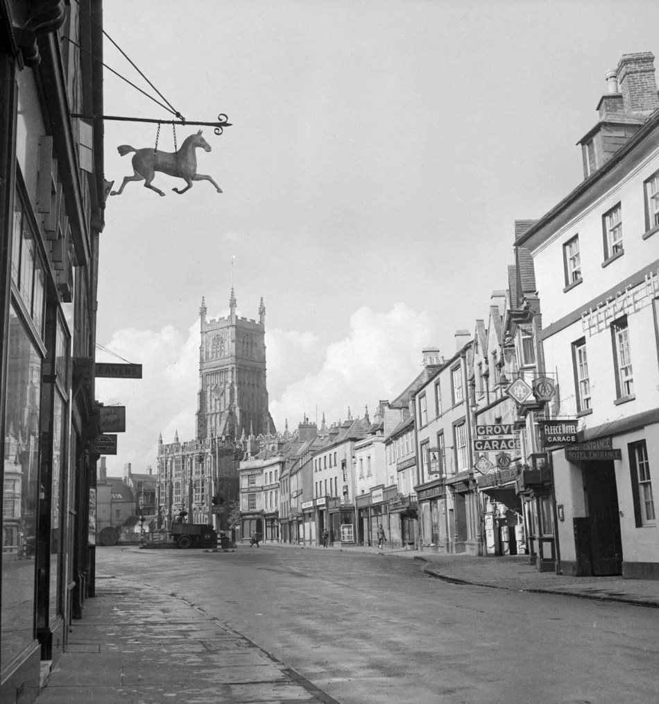 A black and white photograph of a historic high street with a church at the end of the road.