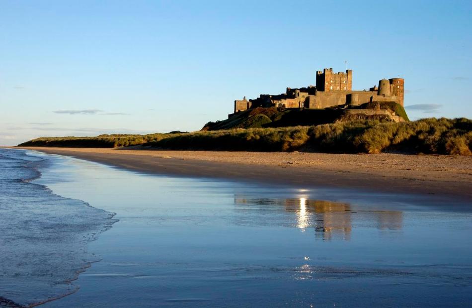 A photograph of a castle on a hill, overlooking a beach.