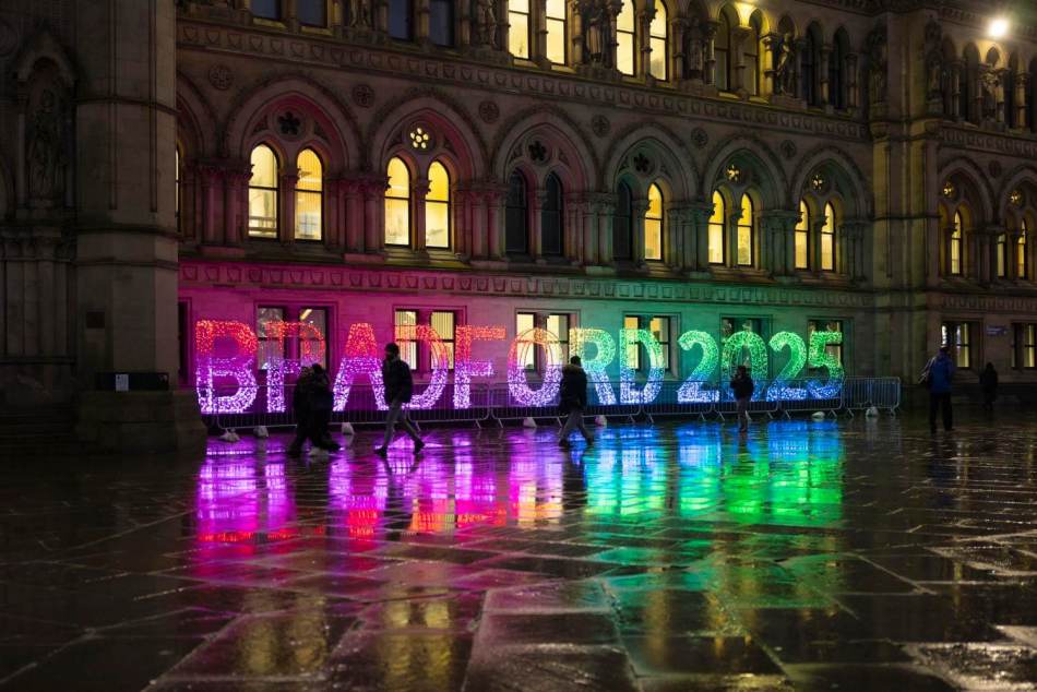 A photograph of a large light installation outside a town hall building at night. The lights are shaped to say 'Bradford 2025'.