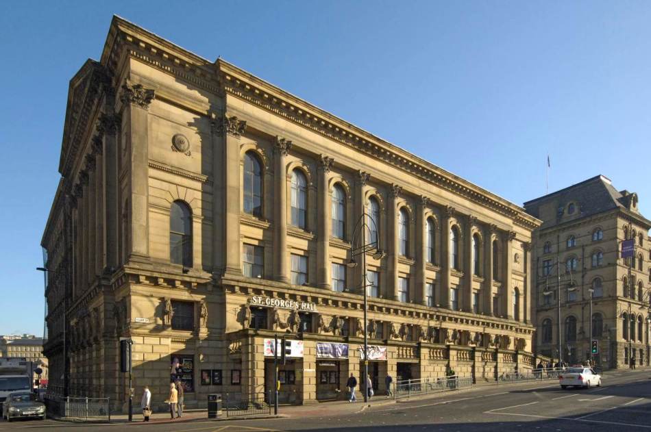 A photograph of the exterior of a large, neoclassical-style concert hall beside a road.
