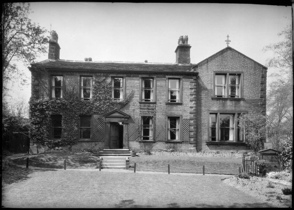 A black and white photograph of the exterior of a large parsonage with ivy growing on the building, surrounded by gardens.