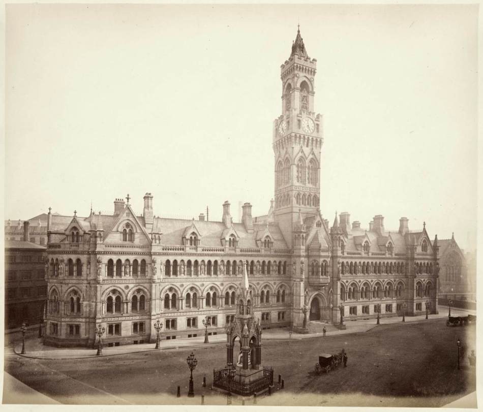 A black and white photograph of a large civic building with a tall clock tower at the centre.