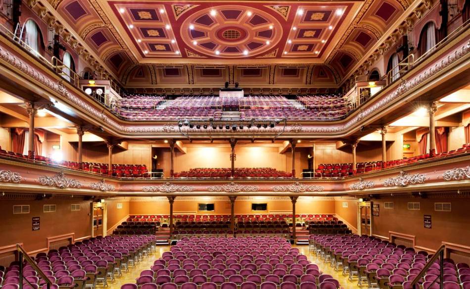A photograph of the interior of a concert hall shot from the stage overlooking 3 levels of seating in the auditorium. 