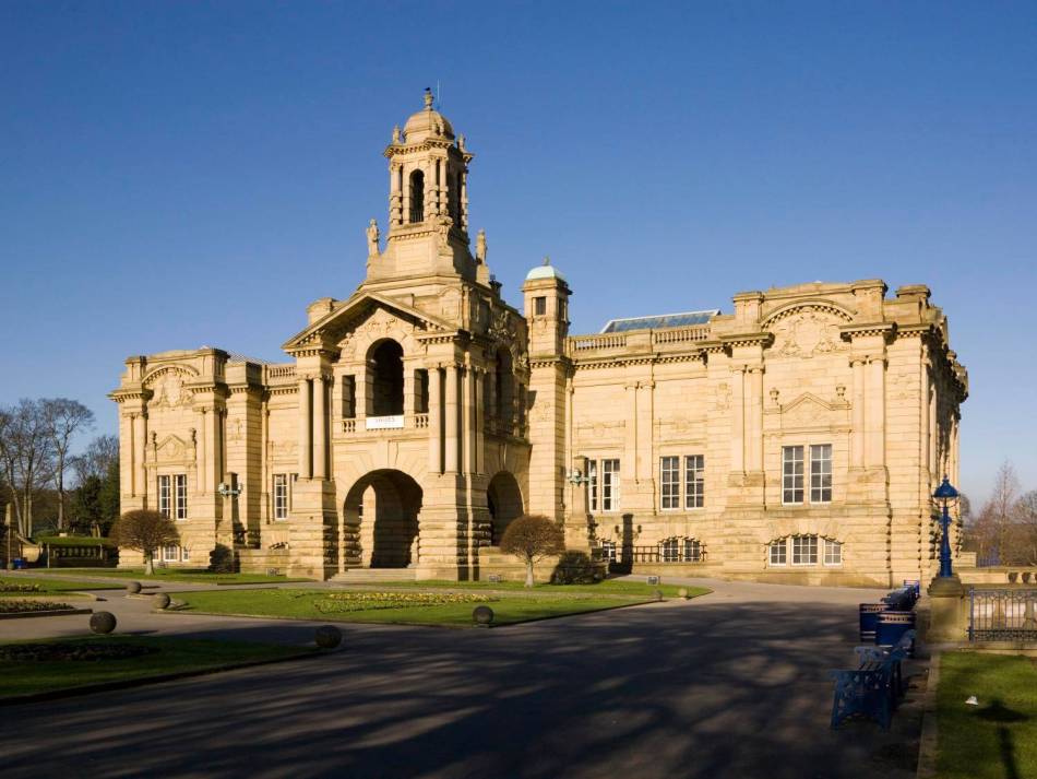 A photograph of the exterior of a large neo-Baroque-style building with a hanging balcony surrounded by elegant columns and stonework.