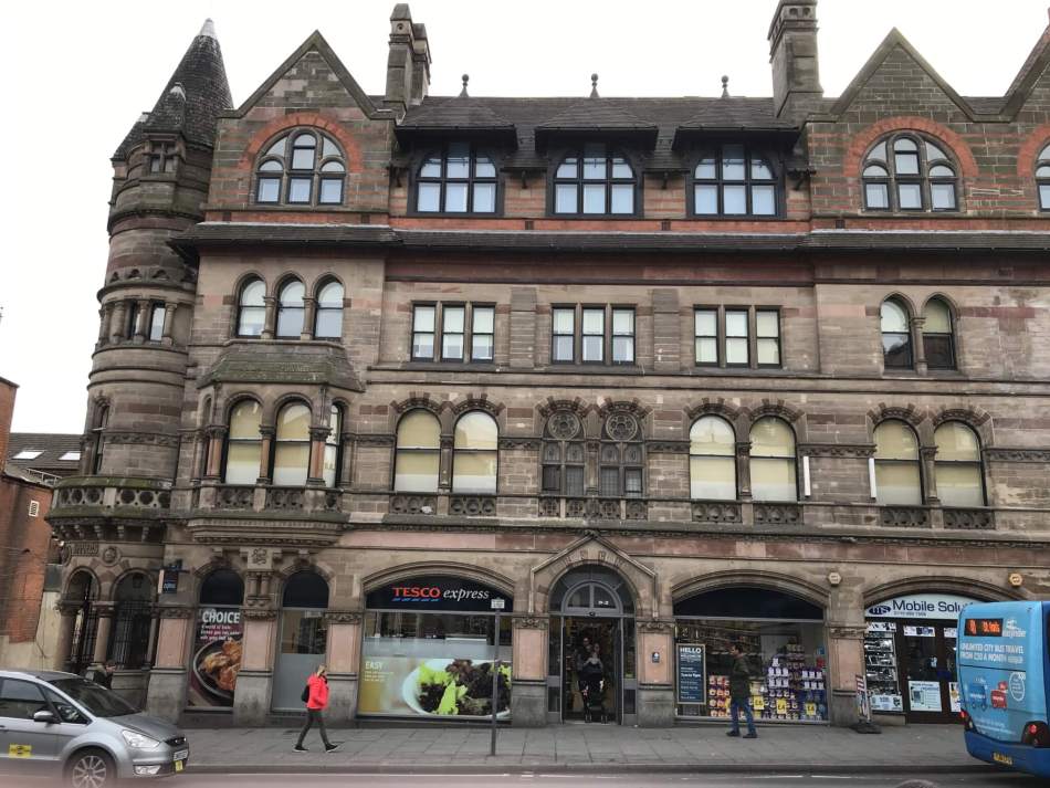 A colour photograph of a large building with several storeys and a Tesco Express underneath. 