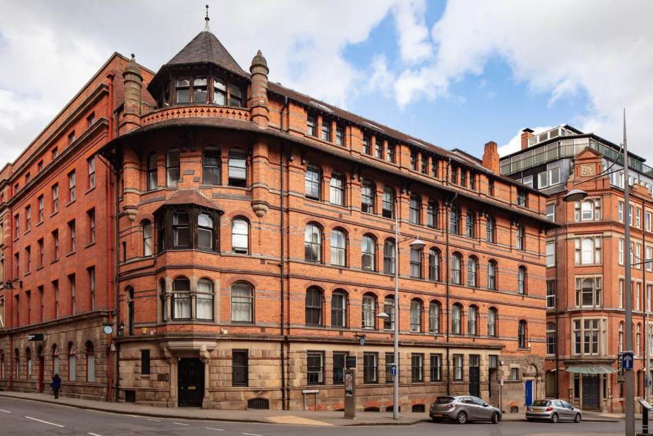 A photograph of the exterior of a converted 5-storey red brick warehouse on the corner of a road.