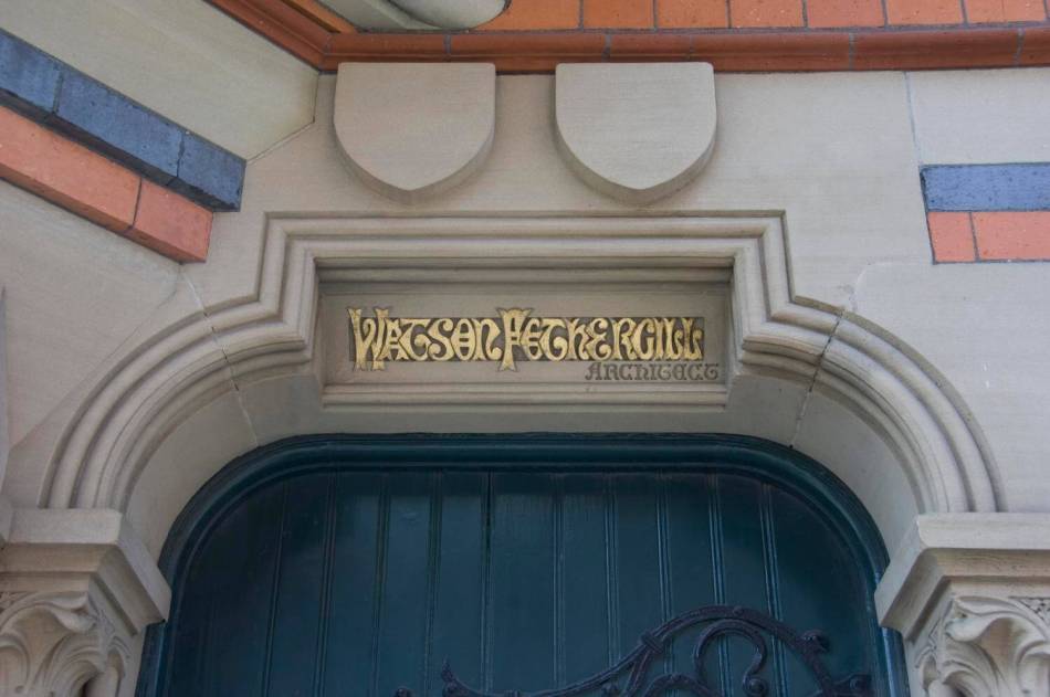 The arch of a doorway with an ornately carved gold sign that reads "Watson Fothergill, architect." 