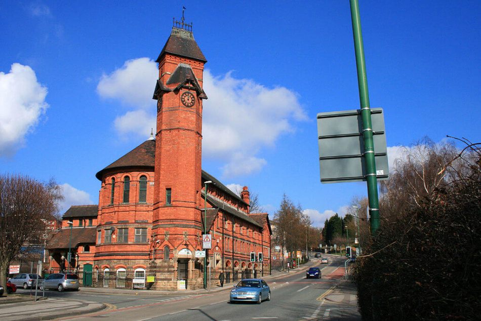 A photograph of a large red brick building on the corner of a road with a tall clock tower.