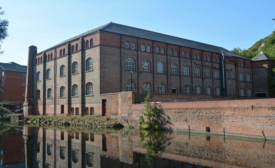 A colour photograph of a large industrial building along a river bank.