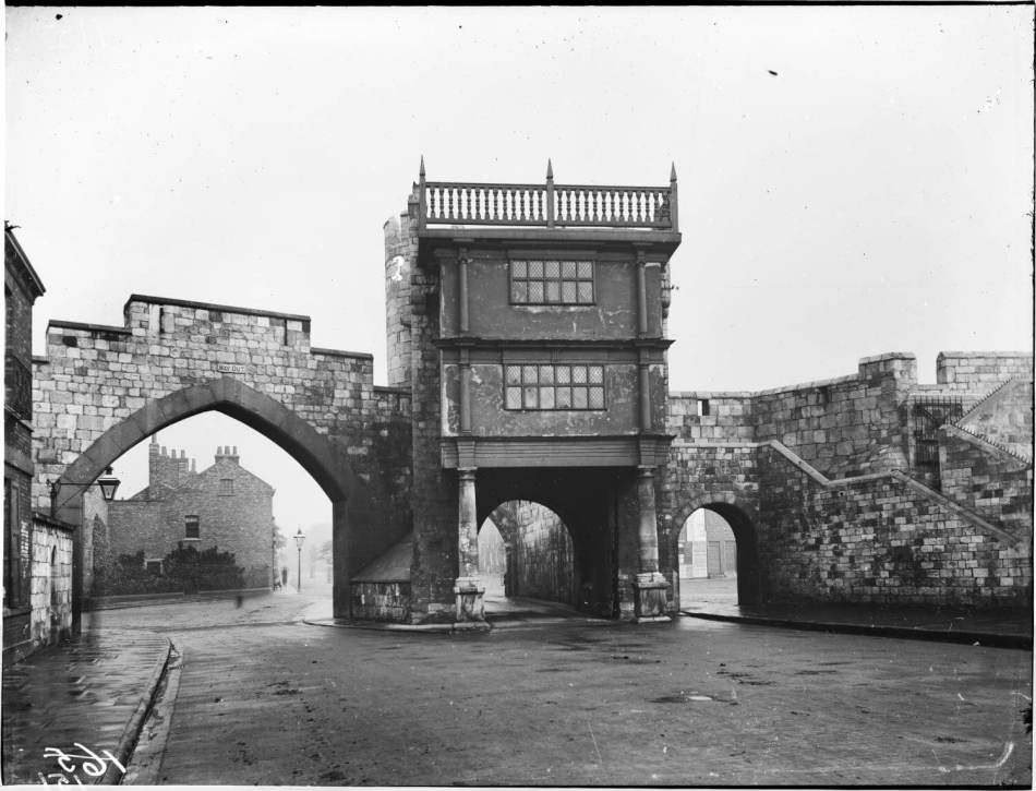 A black and white photograph of a city wall with a grand medieval gateway. 