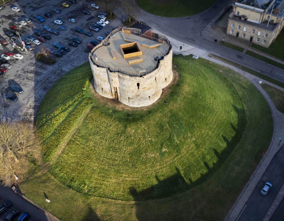 An aerial photograph of a medieval castle ruins on a hill, surrounded by a car park.