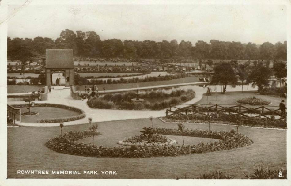 A black and white photograph of a city centre park with formal gardens. 