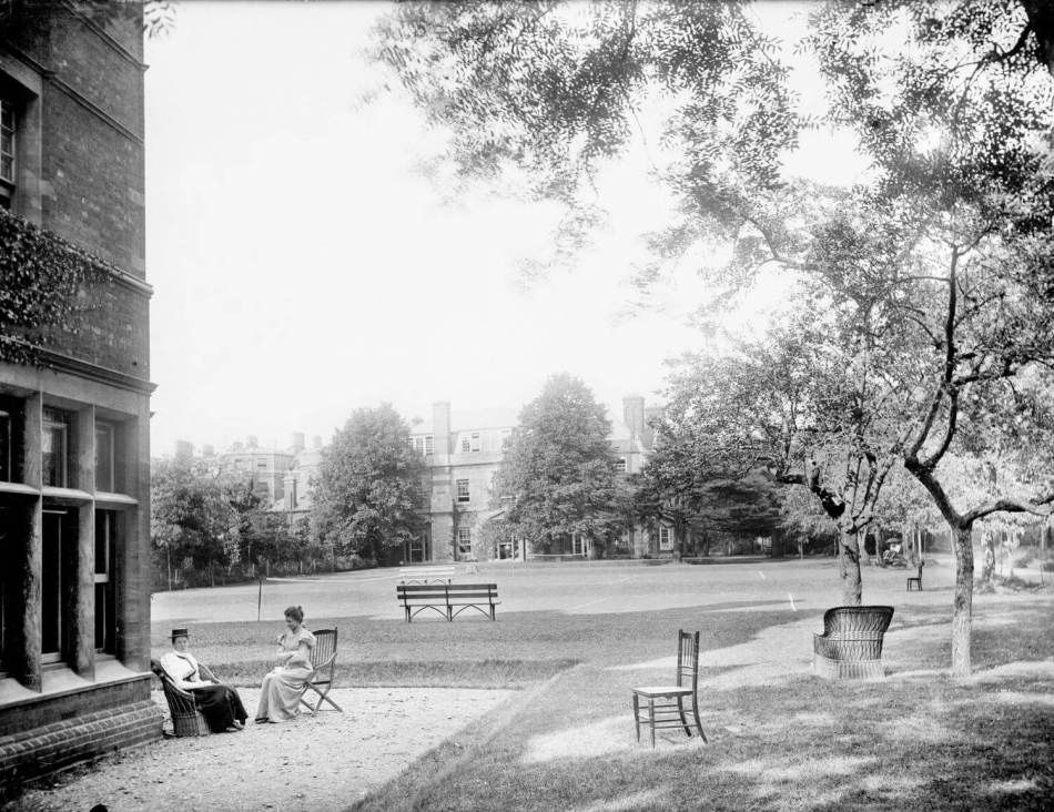A black and white photograph of two women sitting outside of a large building. 