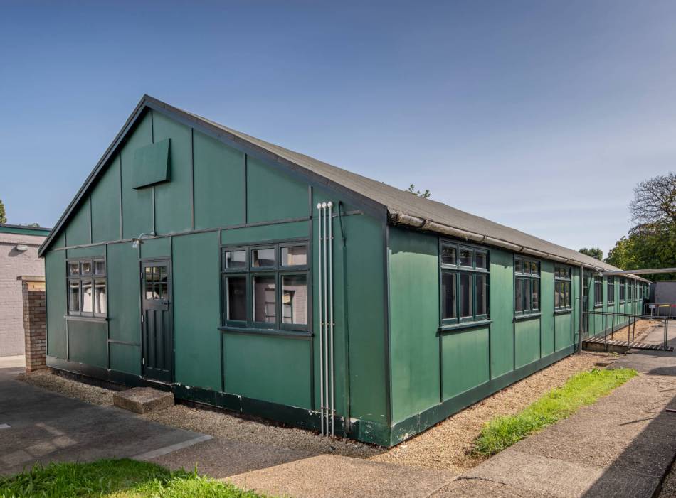 A photograph of a long green hut against a blue sky.