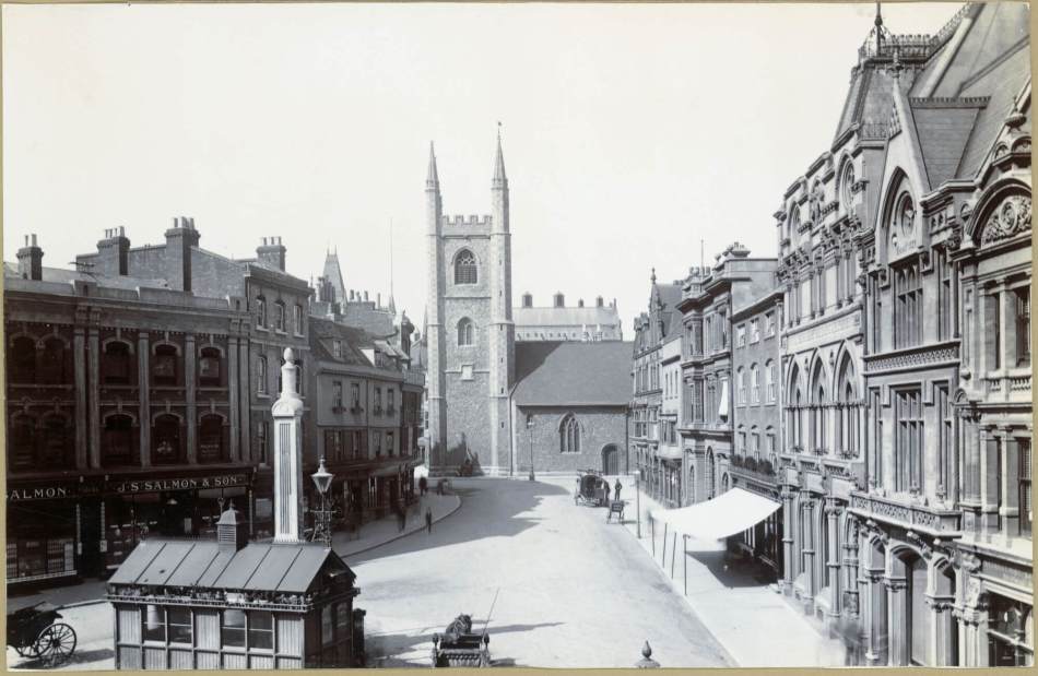 A black and white photograph a historic high street with a church tower in the background.