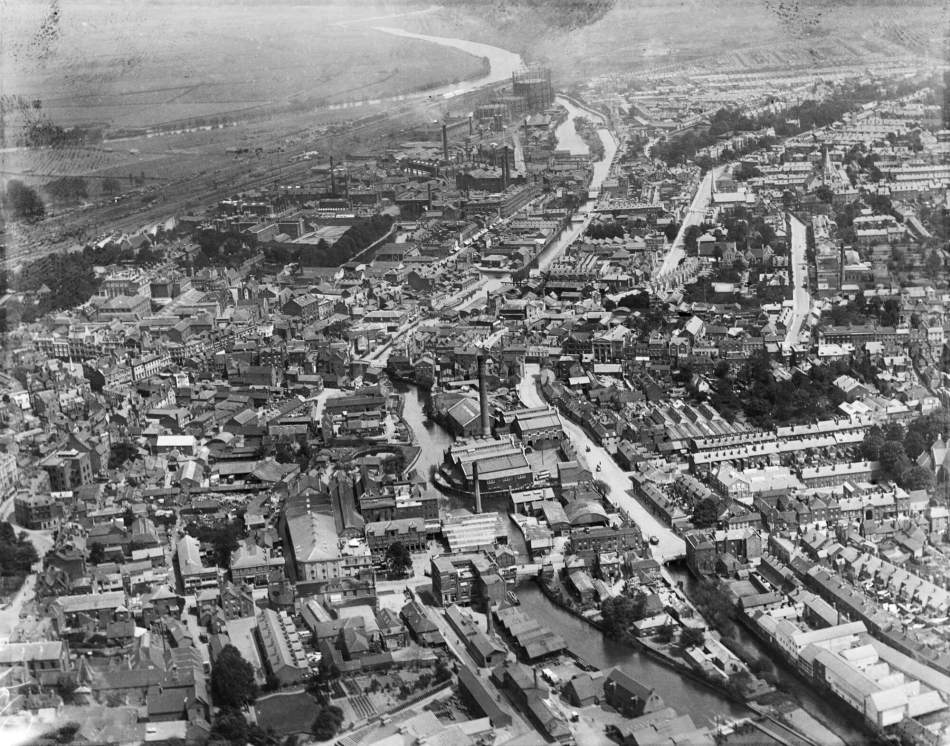 A black and white aerial photograph of an industrial town with a large factory building at its centre.