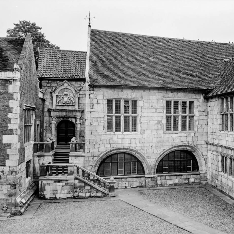 A black and white photograph of medieval brick manor with with large arched windows.