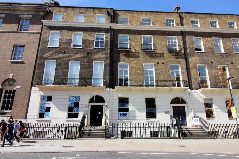 A photograph of the exterior of a terrace of 4-storey town houses beside a road.