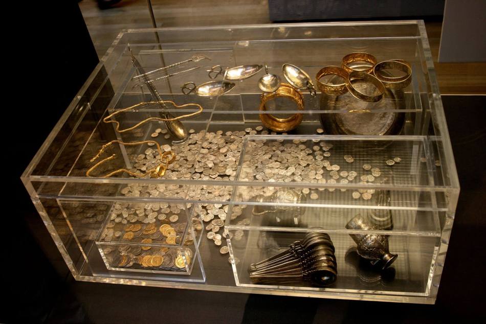 A photograph of a museum case with artefacts from an archaeological treasure hoard including coins, spoons and vessels.