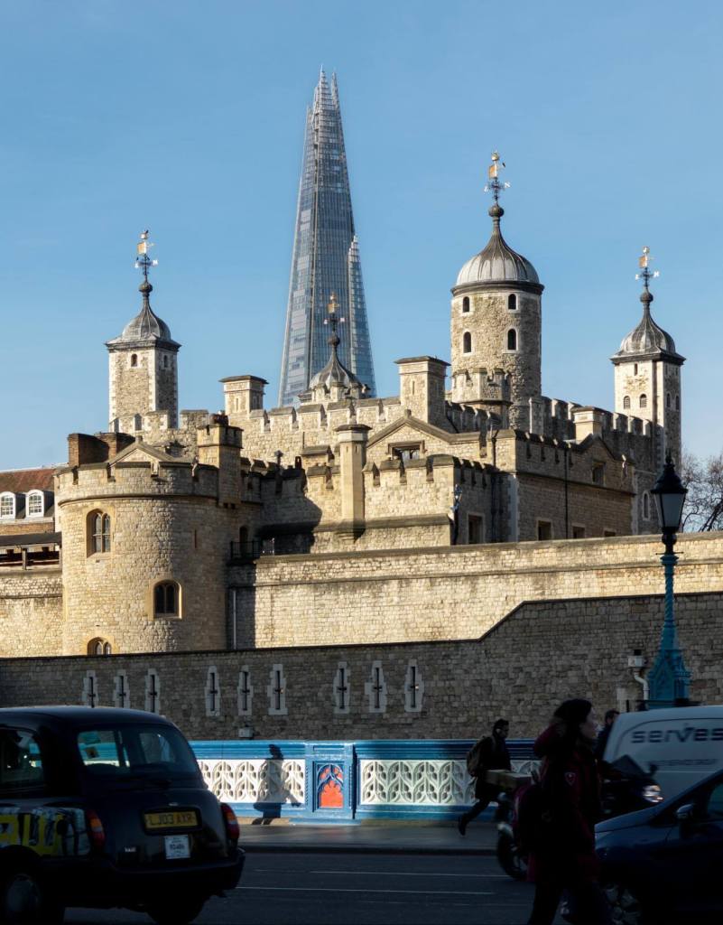 A photograph of a medieval castle surrounded by later walls, with a 20th century sky-scraper in the background.
