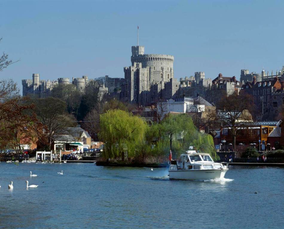 A photograph of a massive castle seen from across a river with a speed boat going past.