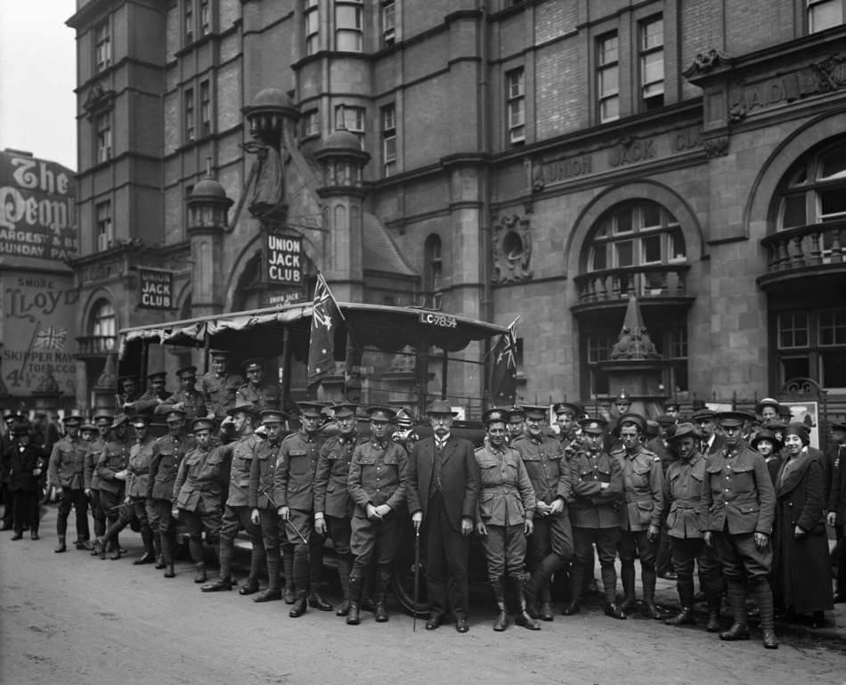A black and white photograph of a group of soldiers in uniform standing outside a large historic building.