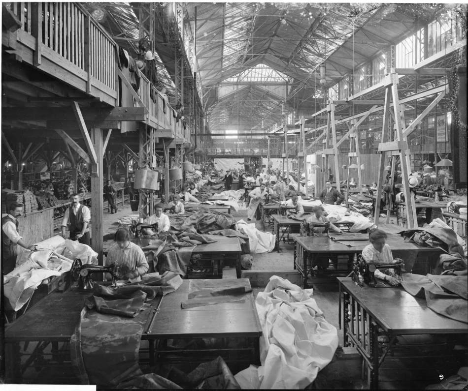 A black and white photograph of a busy factory with women sitting at sewing machines.