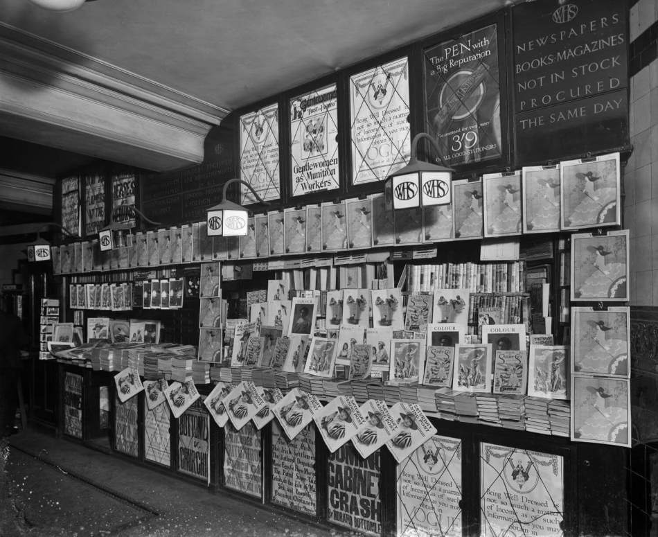 A black and white photograph of a bookstall filled with books, posters and magazines.