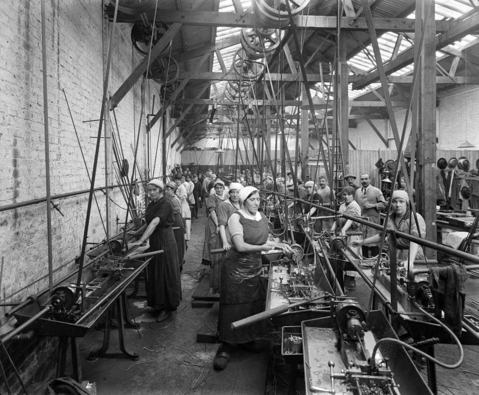 A black and white photograph of a group of workers standing beside machinery in a workshop.