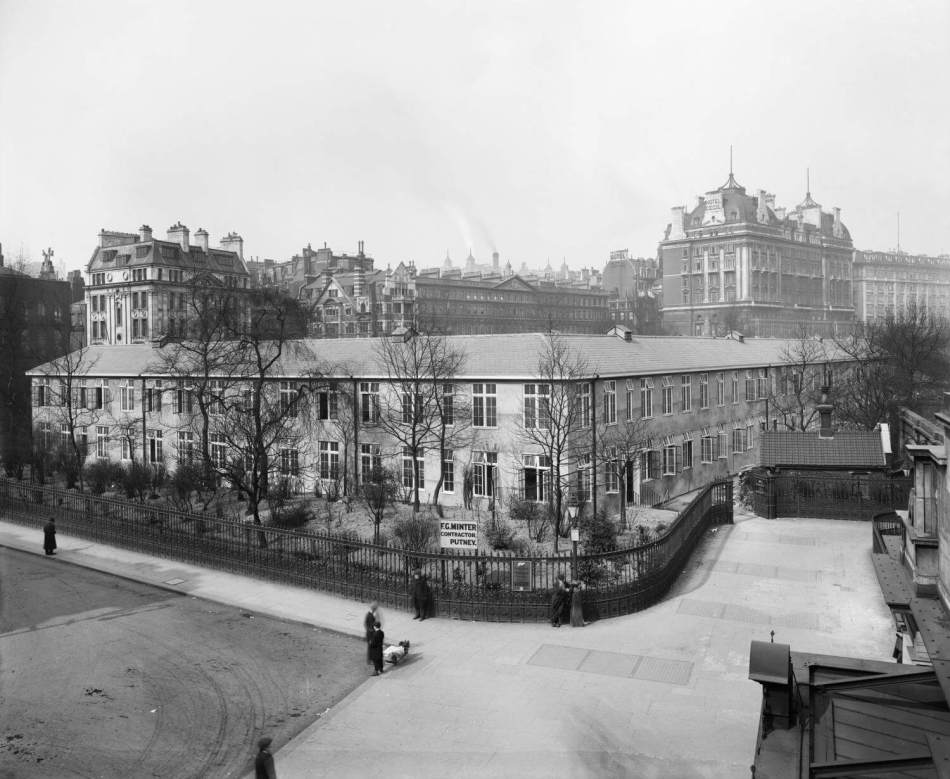 A black and white photograph of a large 2-storey building surrounded by railings.