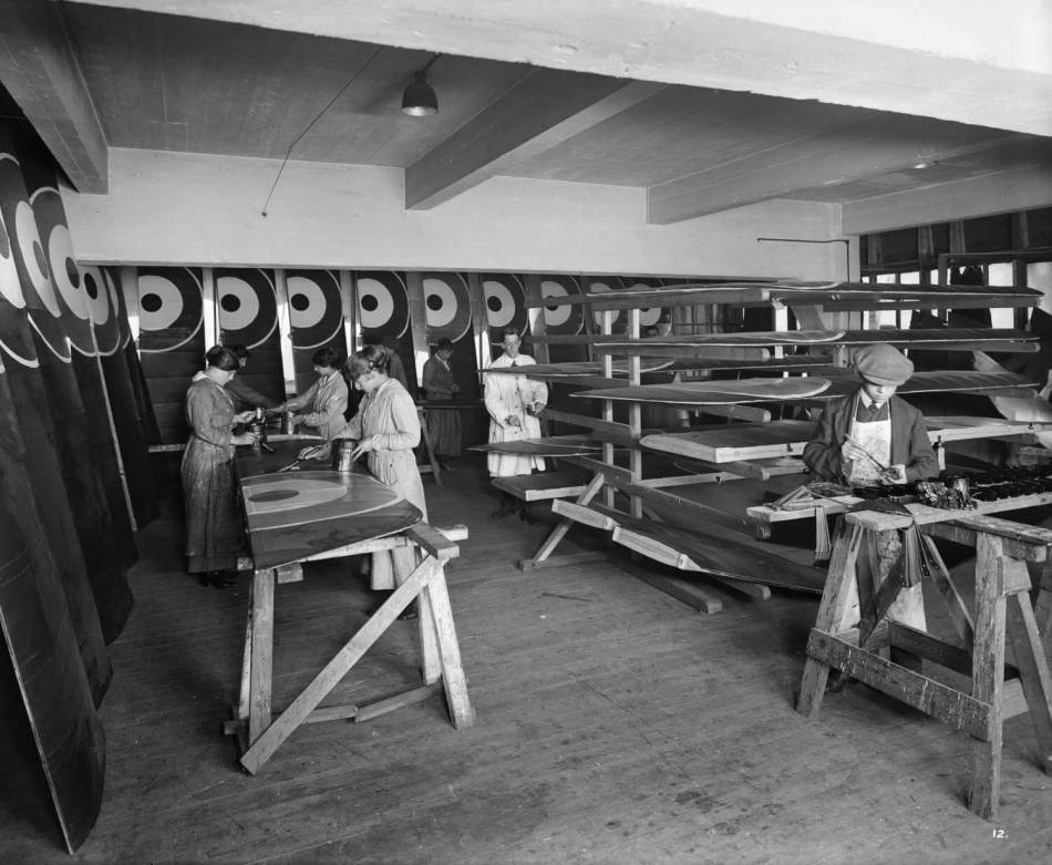 A black and white photograph people working on aircraft wings in a workshop.