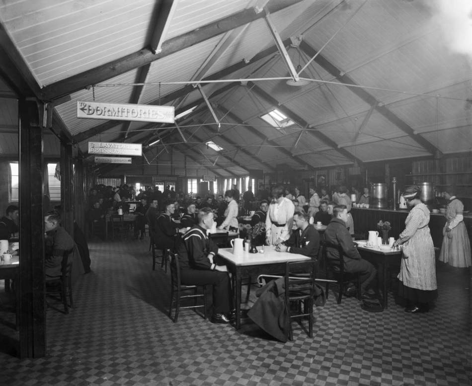 A black and white photograph of a dining hall filled with soldiers and sailors sitting at tables.