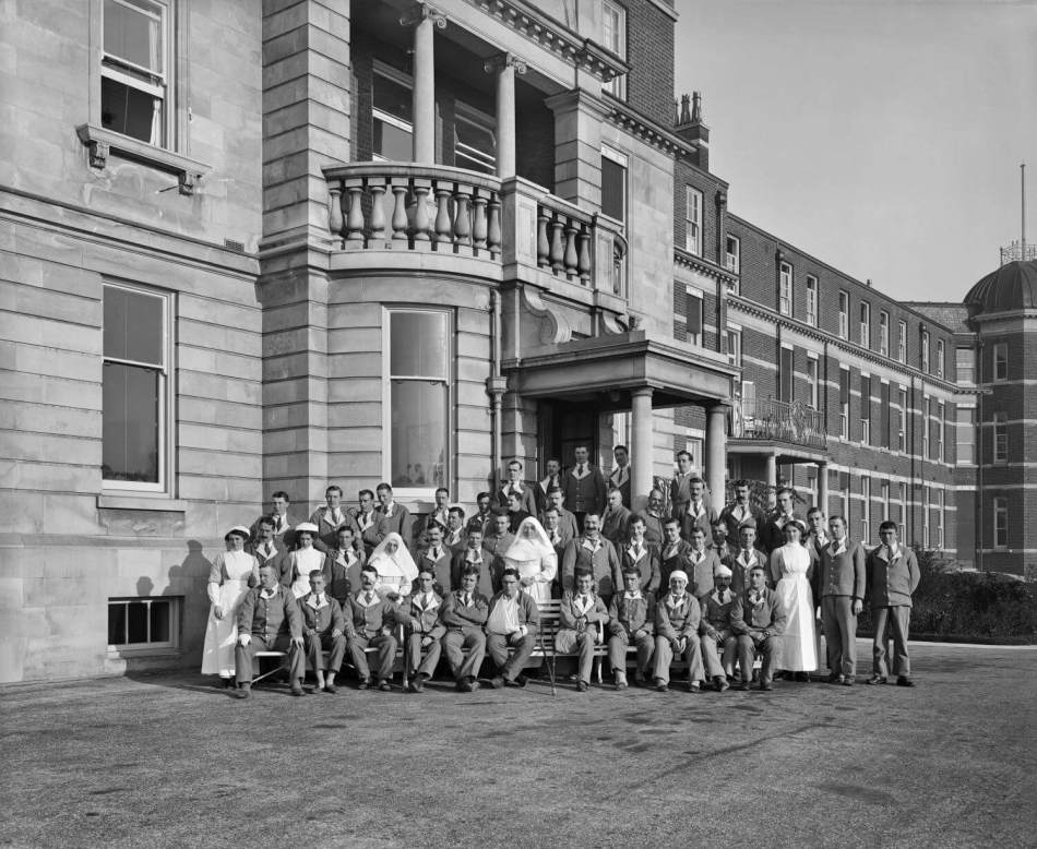 A black and white photograph of a group of patients and hospital staff outside a large hospital building.