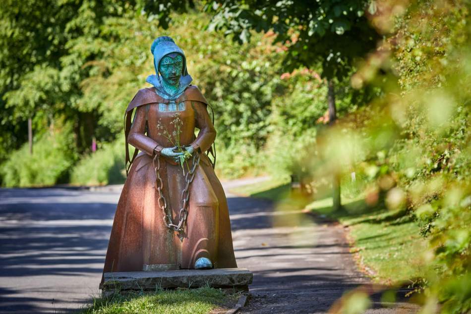 A photograph of a statue of a woman in 17th century dress with chains around her hands. 