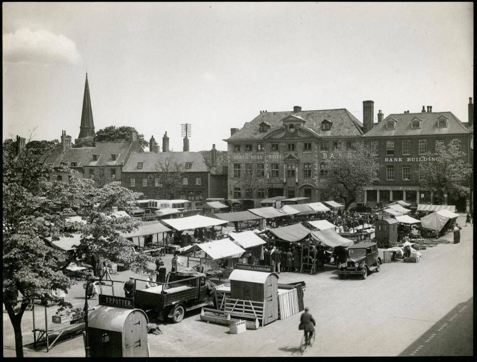 A black and white photograph of a town square with market stalls.