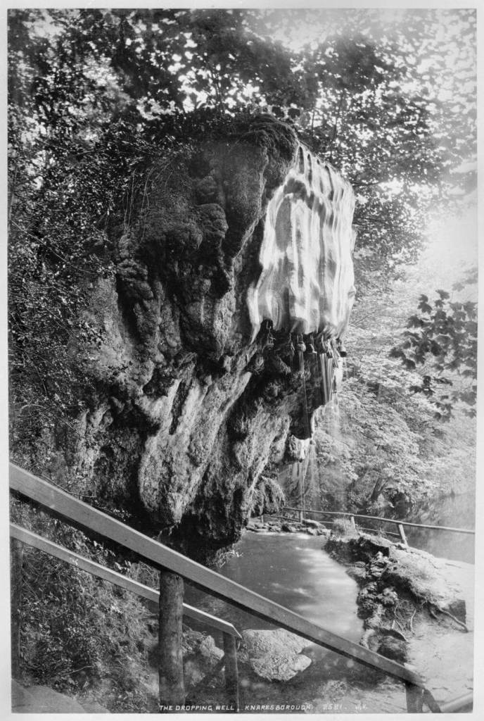 A black and white photograph of a the outside of a cave. 
