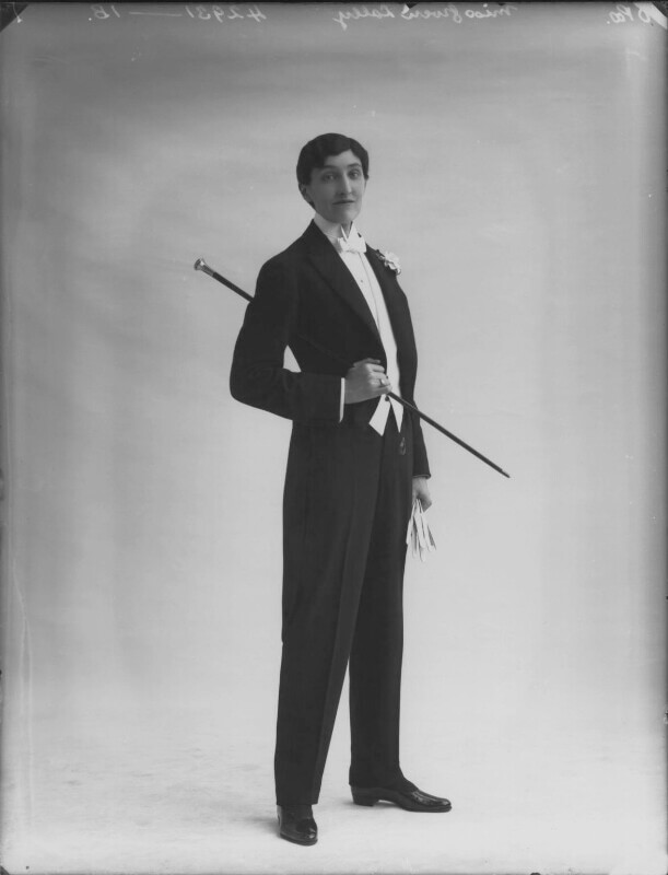 A black and white photograph of a woman with cropped black hair wearing a suit and a cane. 