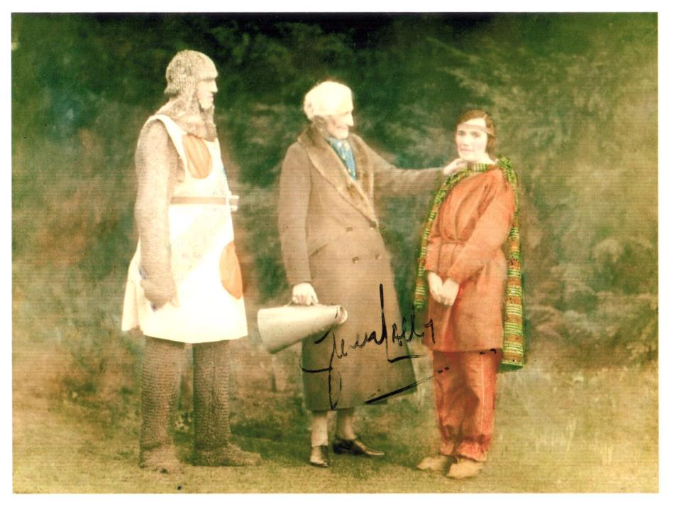 A colourised photograph of two actors in historical costume and in the middle stands a female director holding a megaphone. 