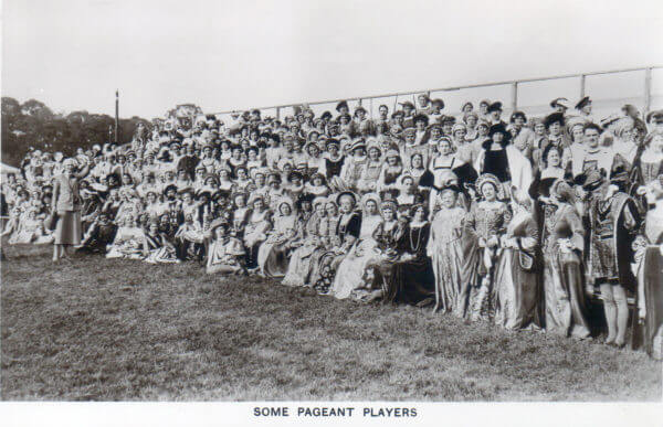 A black and white photograph of a large group of people in a field, many of which are in historical costume. 