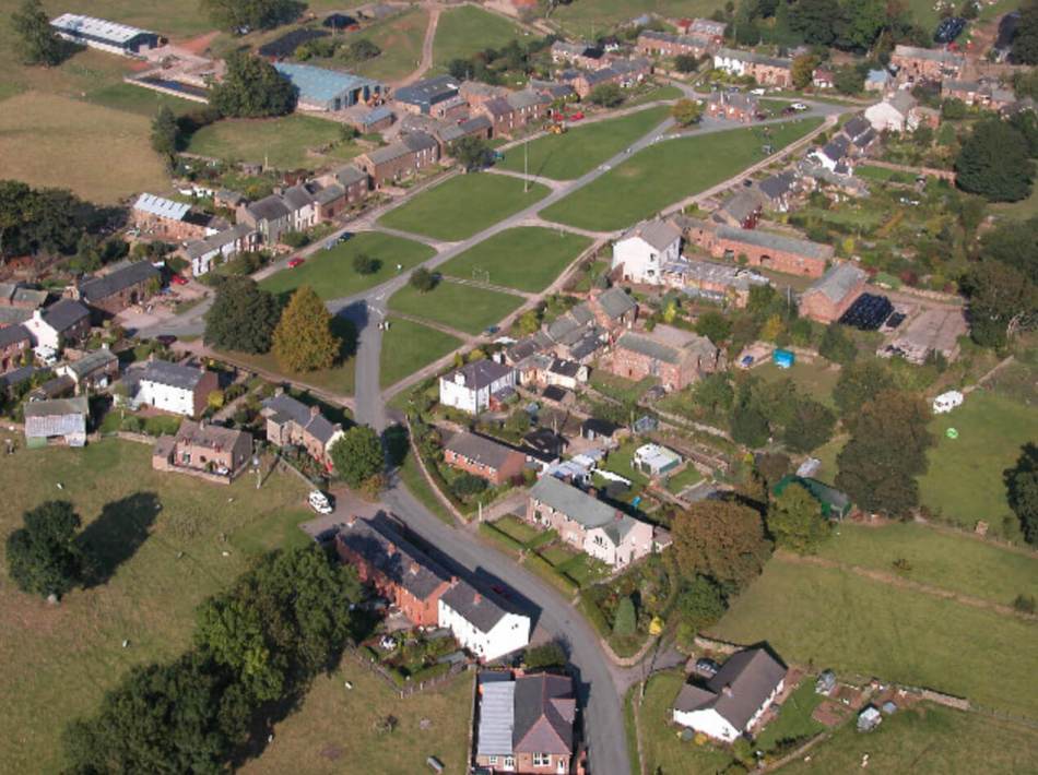 An aerial photograph of a village with rows of cottages and green space at the centre of the village.