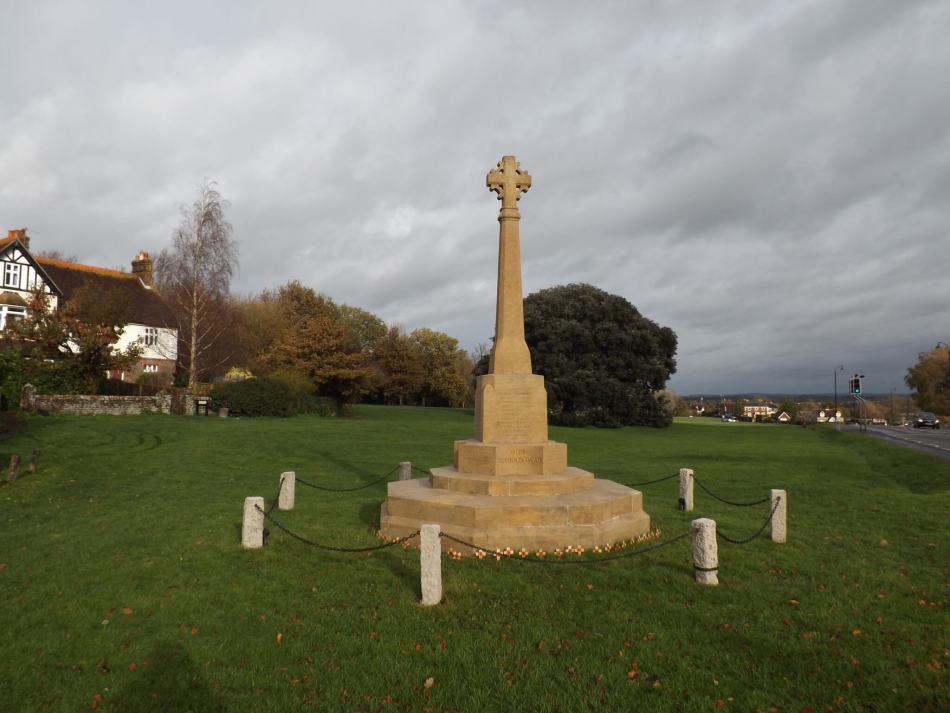 A photograph of a stone war memorial in the middle of a village green.