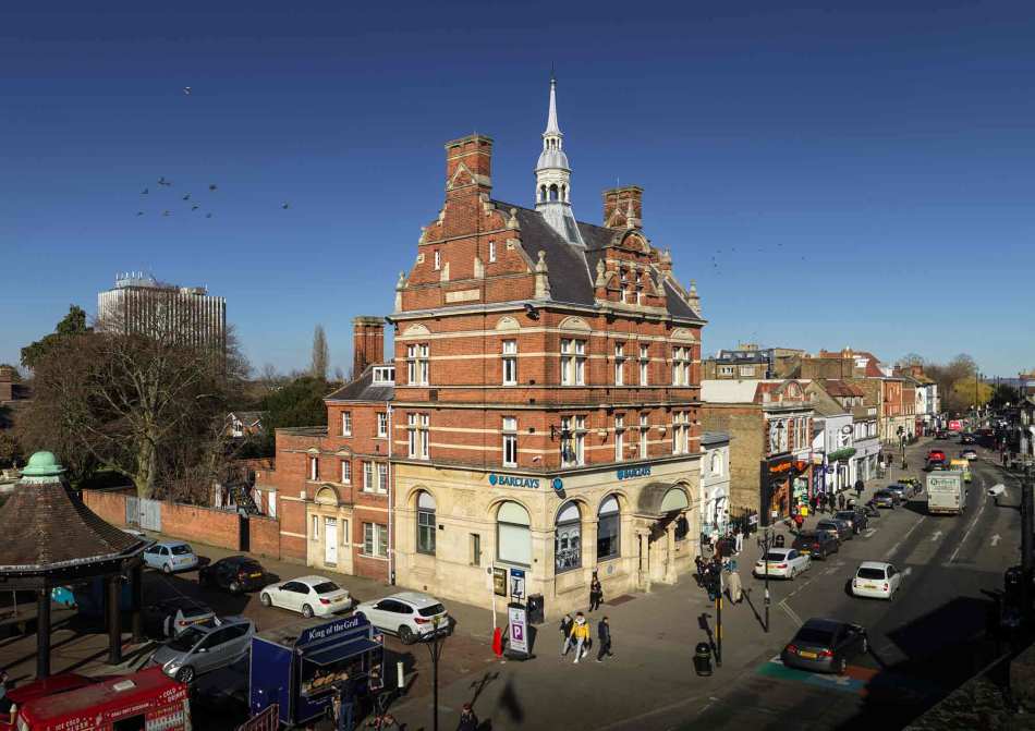 A photograph of a red brick purpose built bank next to a busy junction.