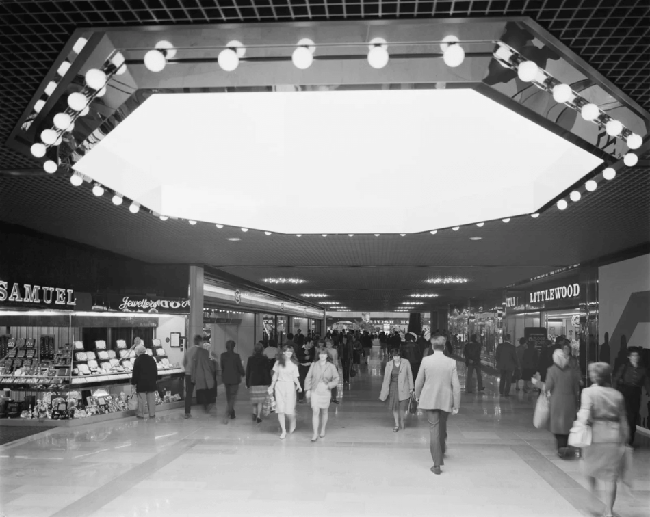 A black and white photograph of a shopping centre in the 1980s.