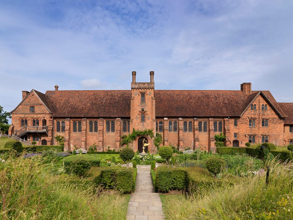 A photograph of a red brick palace surrounded by gardens.