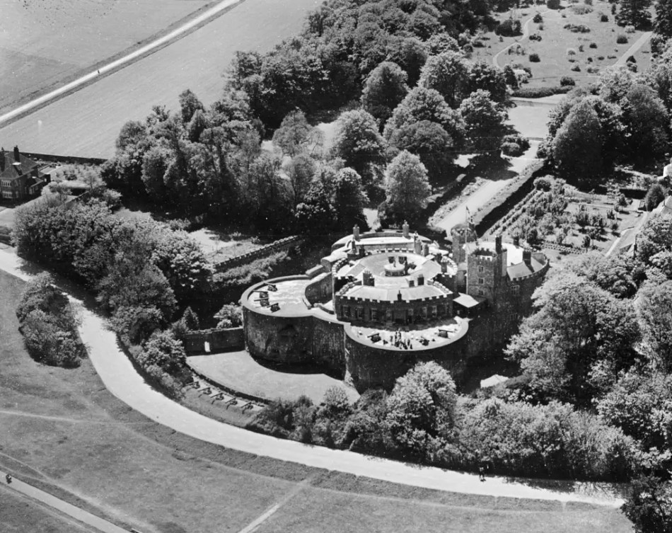 A black and white aerial photograph of a castle surrounded by gardens and trees.