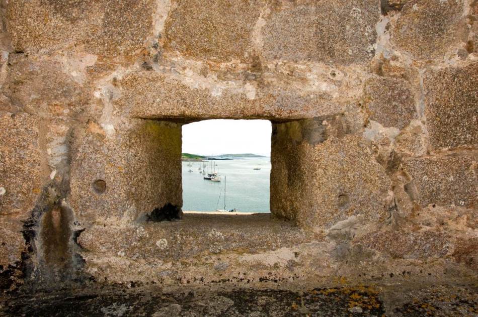 A photograph of a close-up of the wall of a castle with a loophole looking out to the sea.